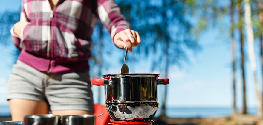 A woman cooks on her camping stove on a picnic table.