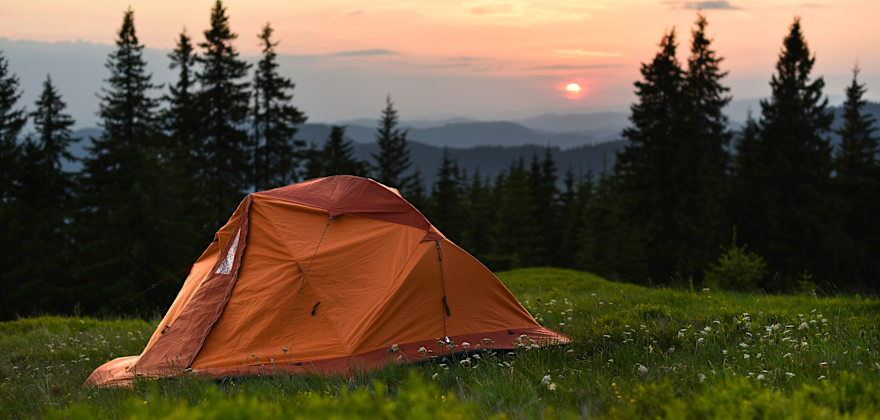 tent on a hill overlooking mountains at sunset.