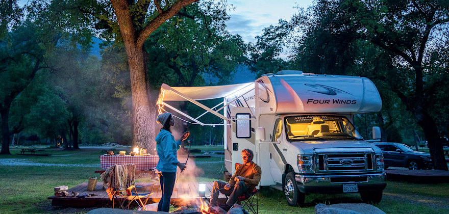 A couple relax around a campfire outside their RV.