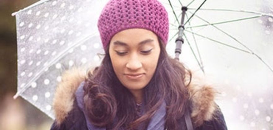 A woman with AAA personal umbrella protection insurance stands under an umbrella in the rain