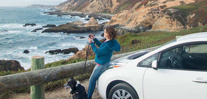 A woman overlooks the Pacifica Ocean alongside her dog and her Nissan Leaf.