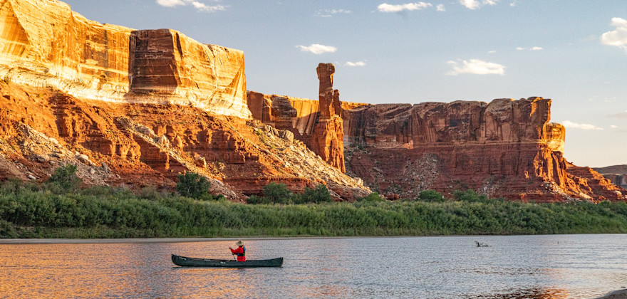 A person paddles up the green river at sunset.