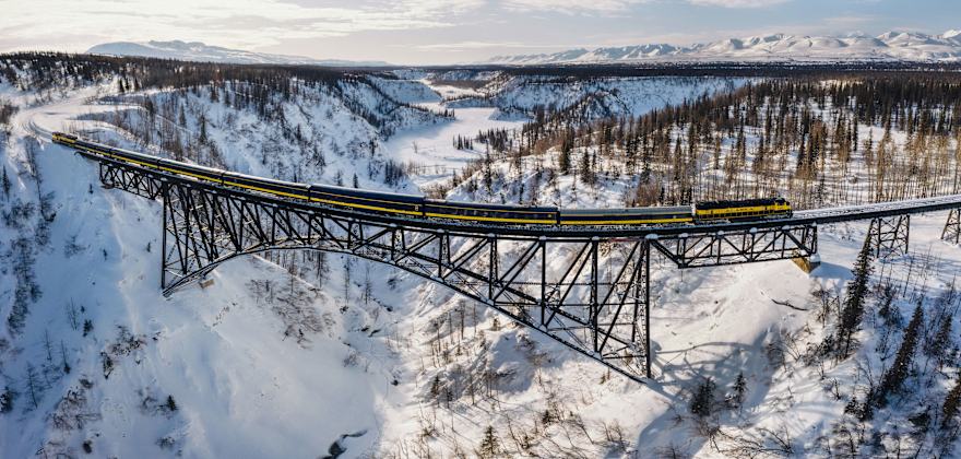The Aurora Winter Train crosses a bridge over a snow-covered valley in Alaska.