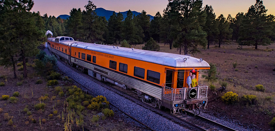 An orange rail car from the Grand Canyon Railway rides the rails.