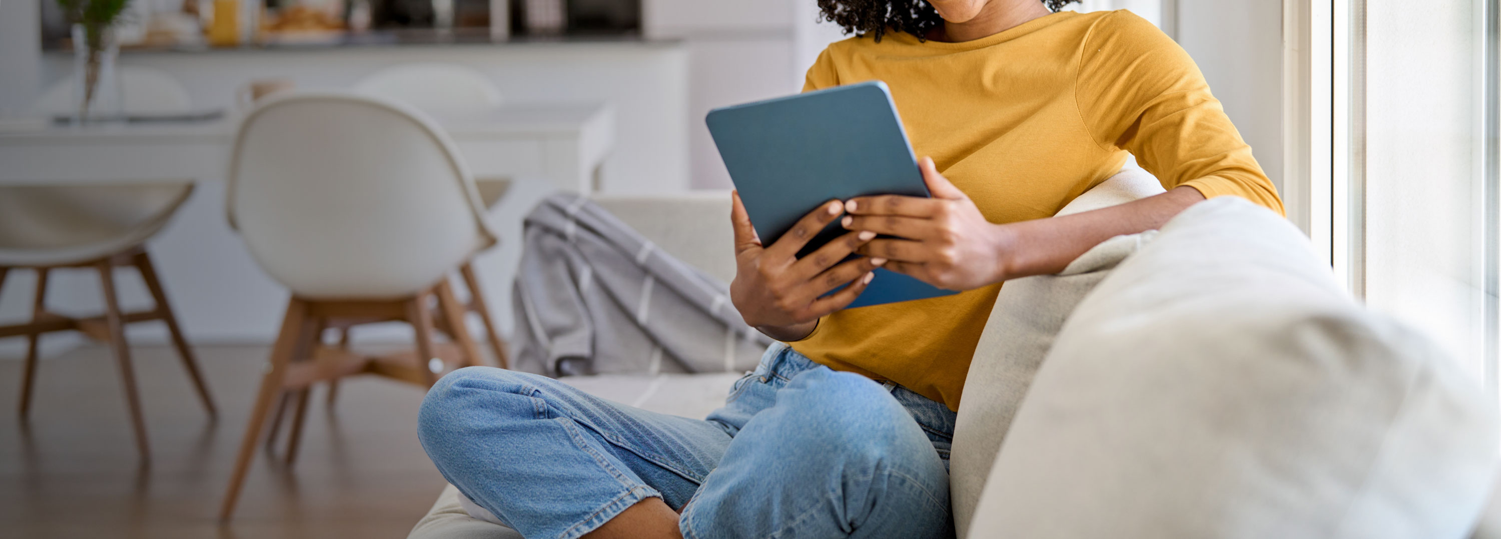 A woman in a yellow shirt reads an issue of Via magazine on her tablet.