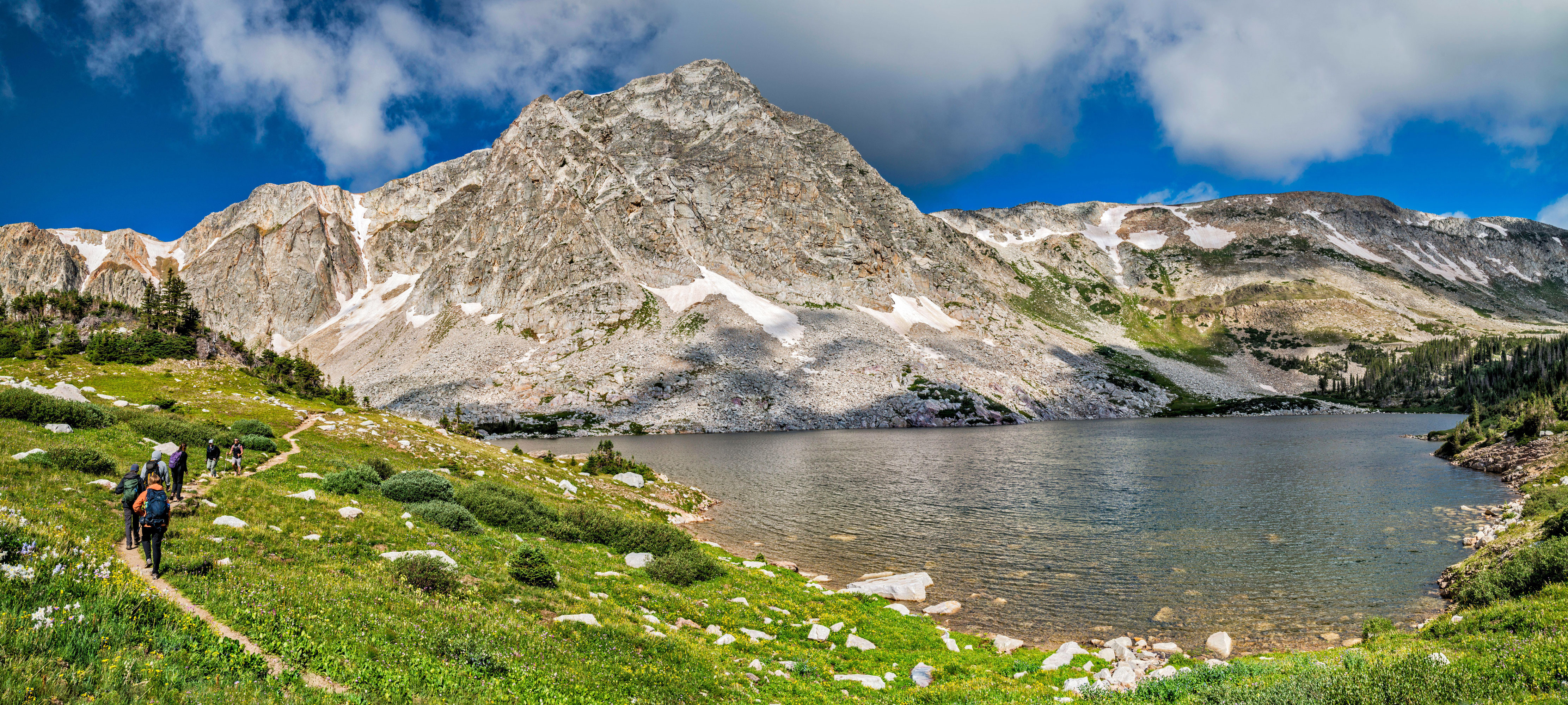 Hikers walk on the Lakes Trail overlooking Lookout Lake with Medicine Bow in the background.