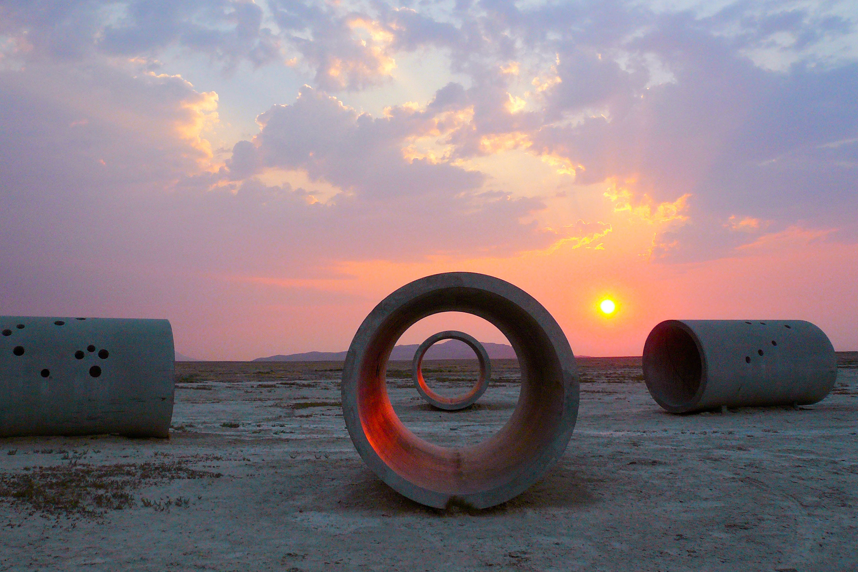 Steel and concrete sculptural structures in the Utah desert at sunset.