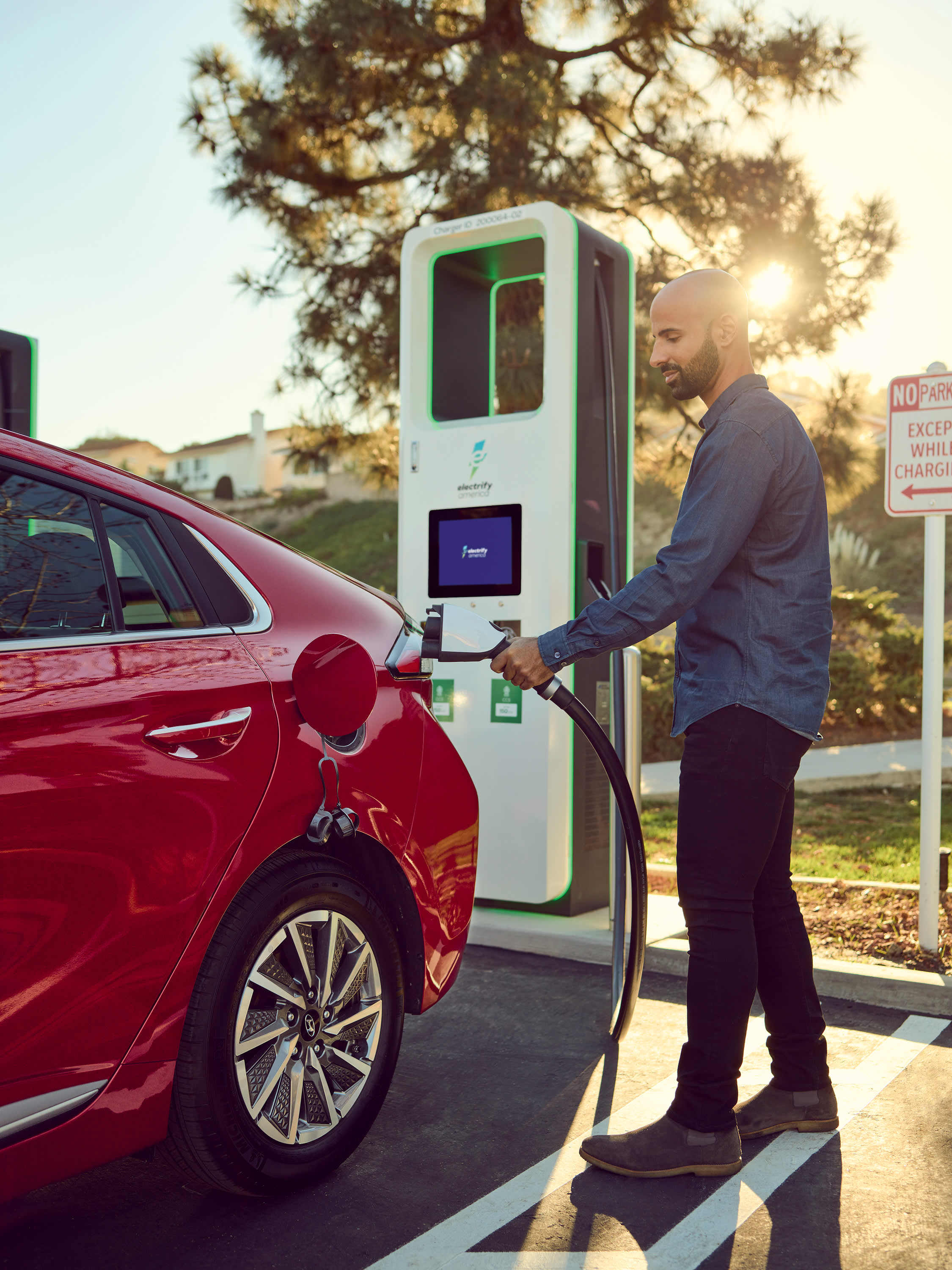 A man plugs in his red EV at an Electrify America fast charger.