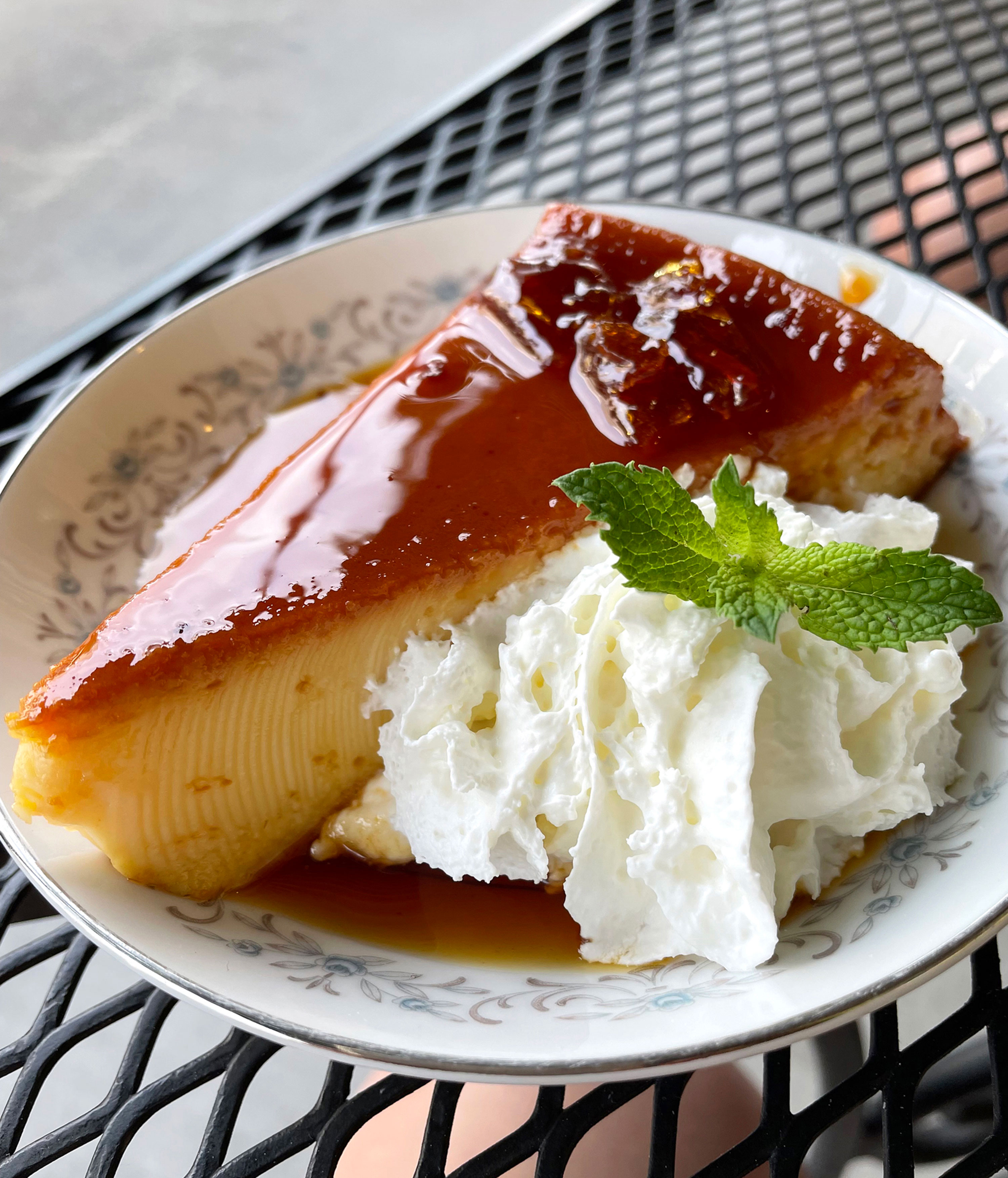 Flan and whipped cream on a table outside of Cultured Palate.