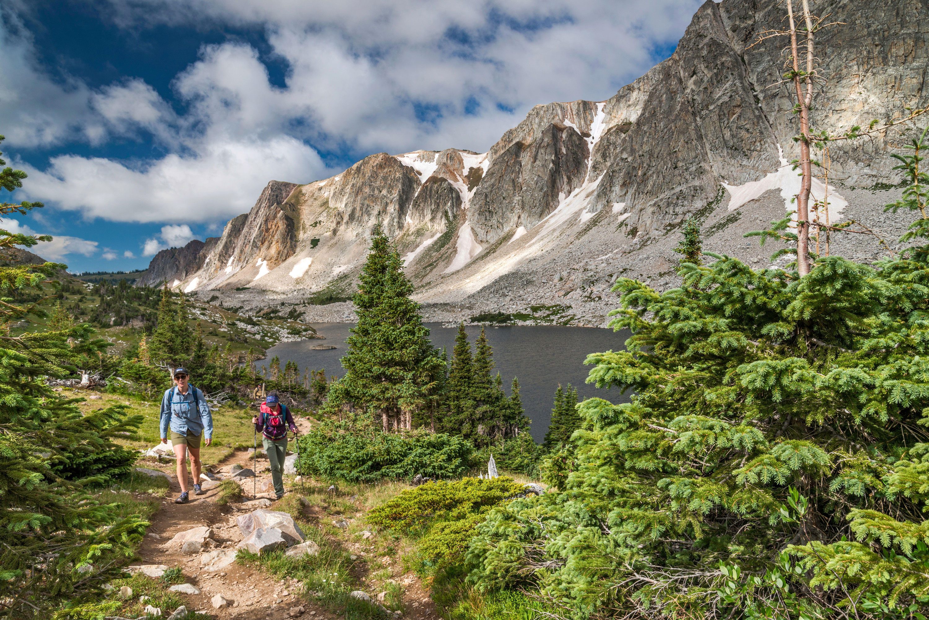 Hikers walk on the Lakes Trail overlooking Lookout Lake with Medicine Bow in the background.