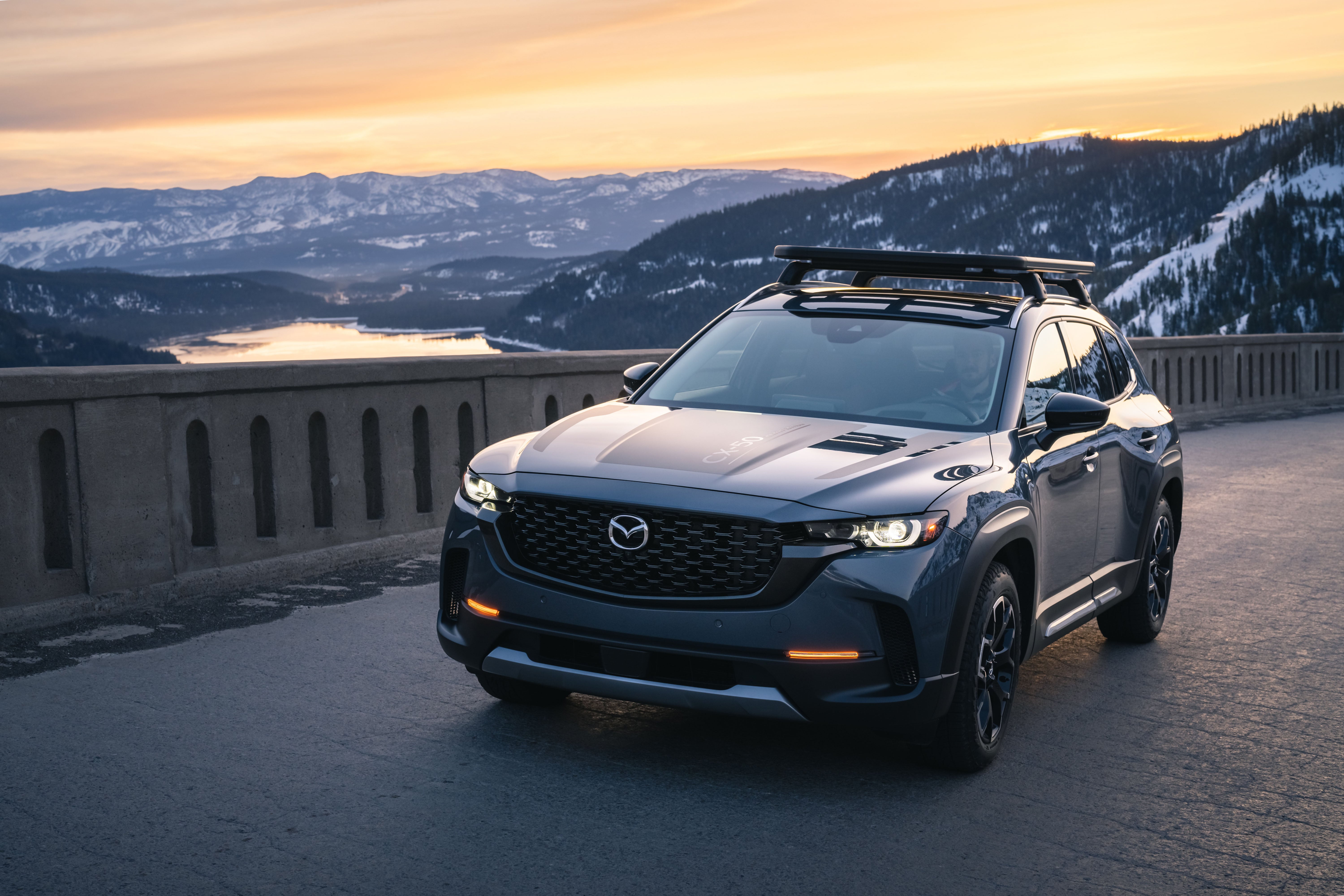 Mazda CX-50 Hybrid climbing a mountain road with snow on the ground in the background.