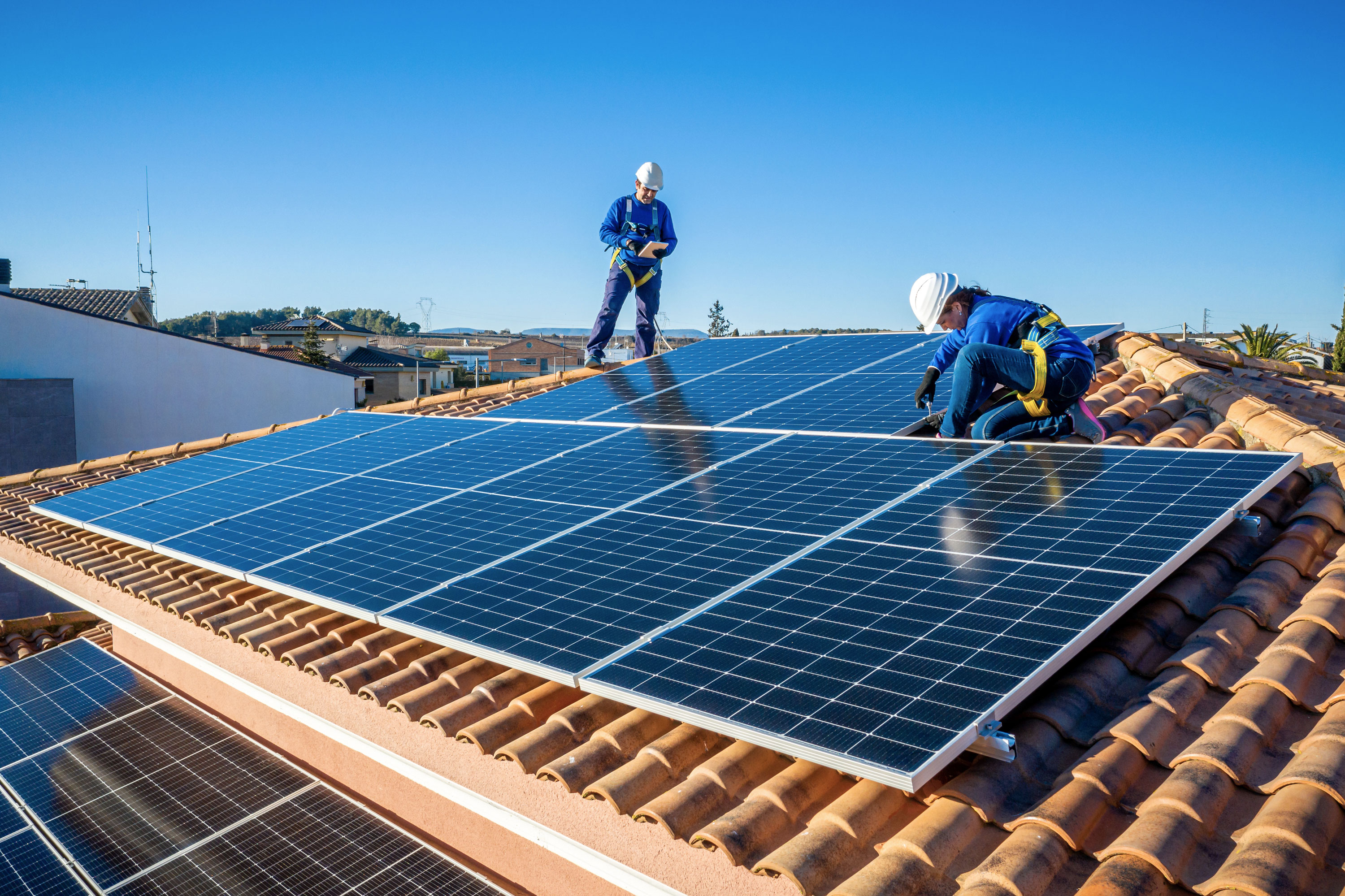 Two workers install solar panels on a home's tile roof.