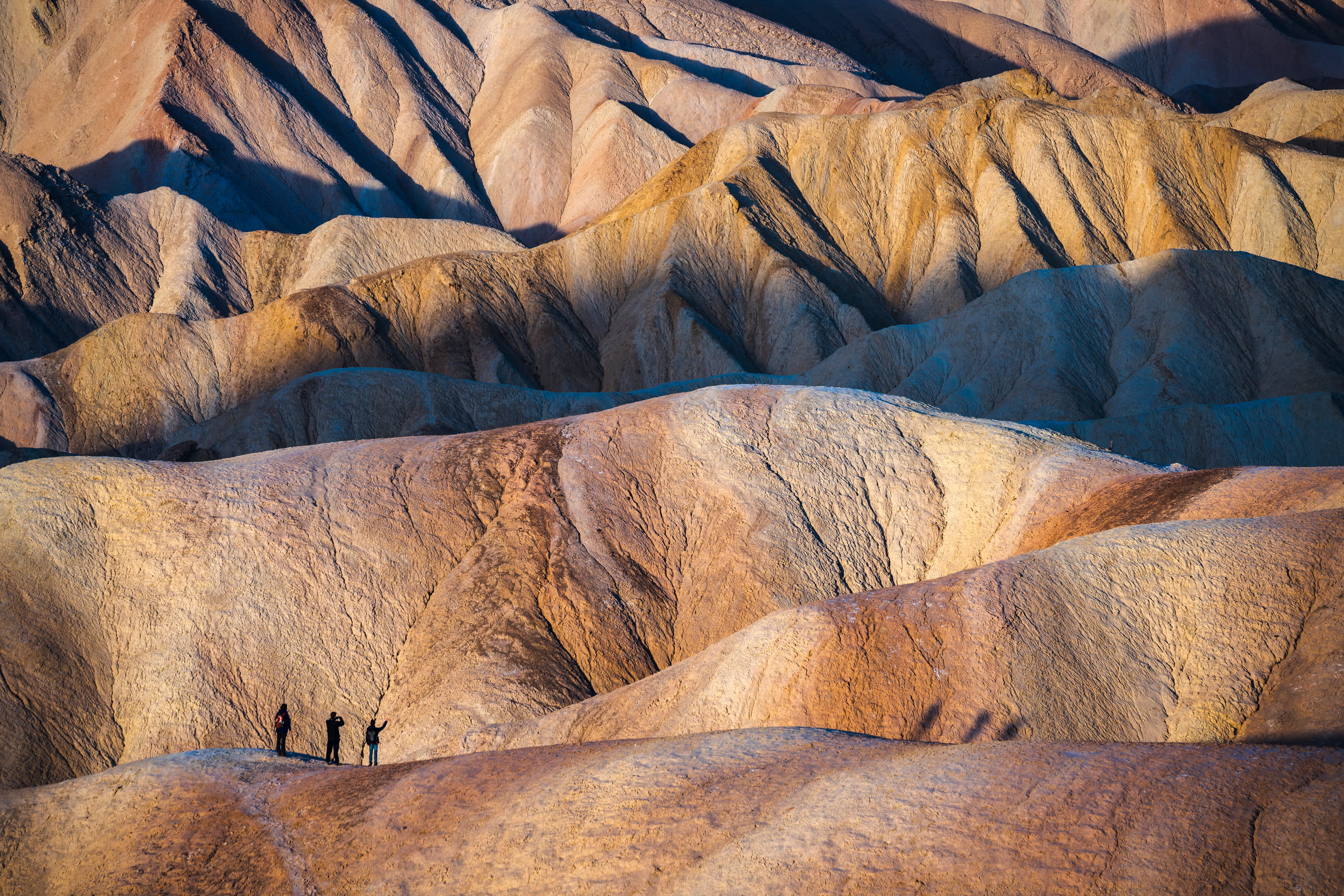 desert badlands with dramatic shadows, and three hikers shot from far away in Death Valley National Park, California