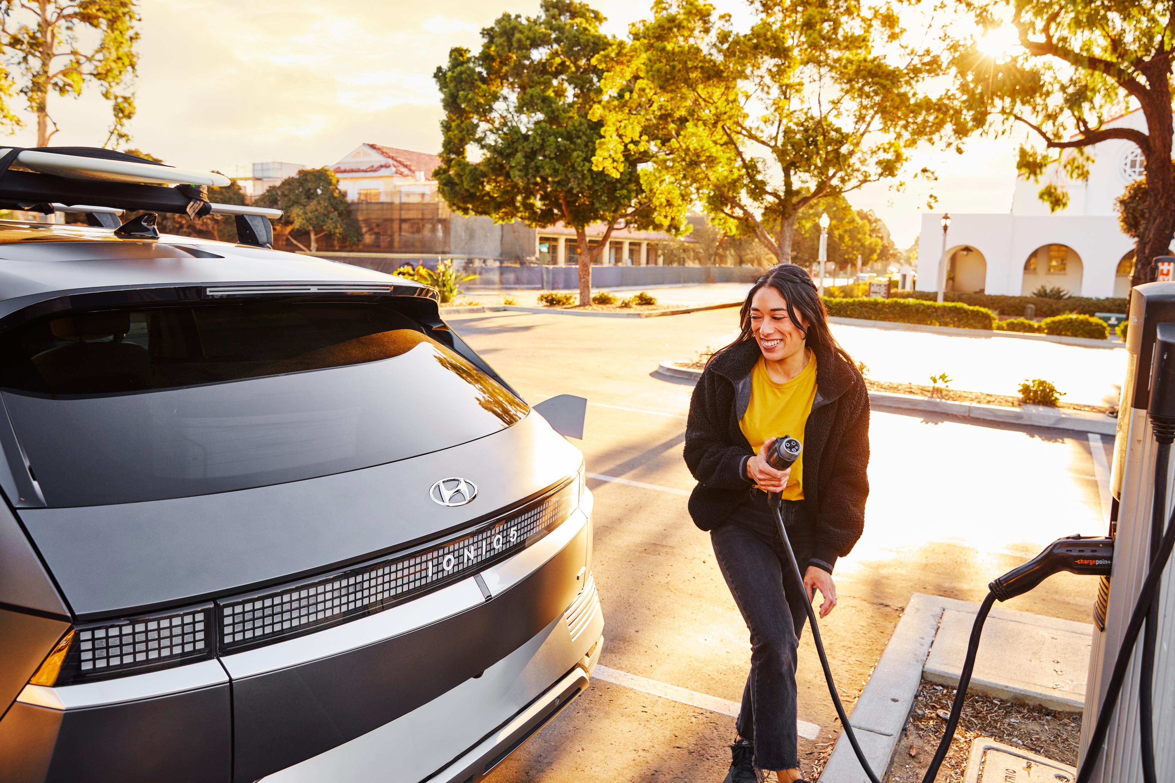 A woman walks an EV charging cable to her Hyundai Ioniq5 EV.