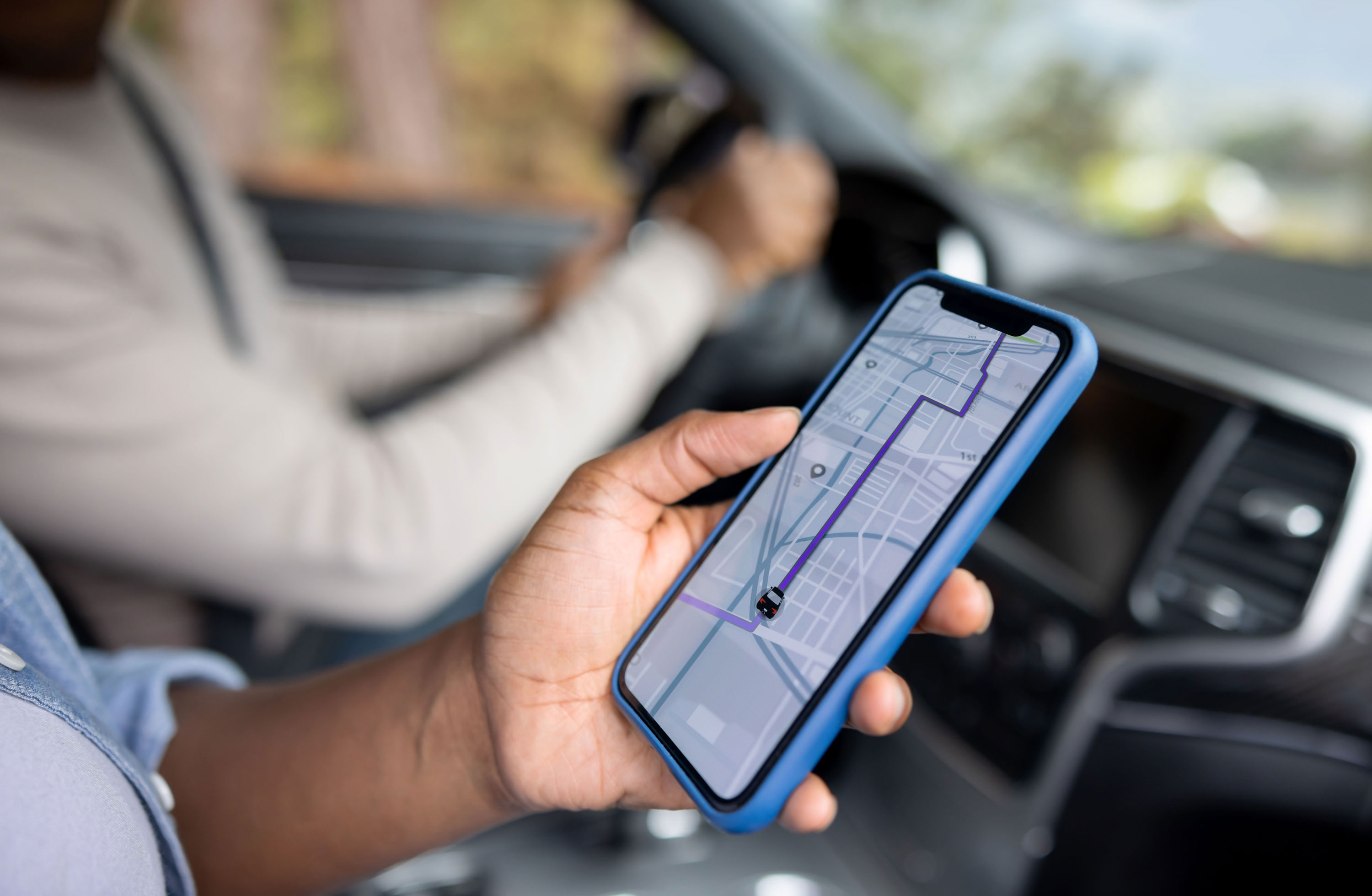 A passenger looks at a GPS map on their phone while another person drives in the background.