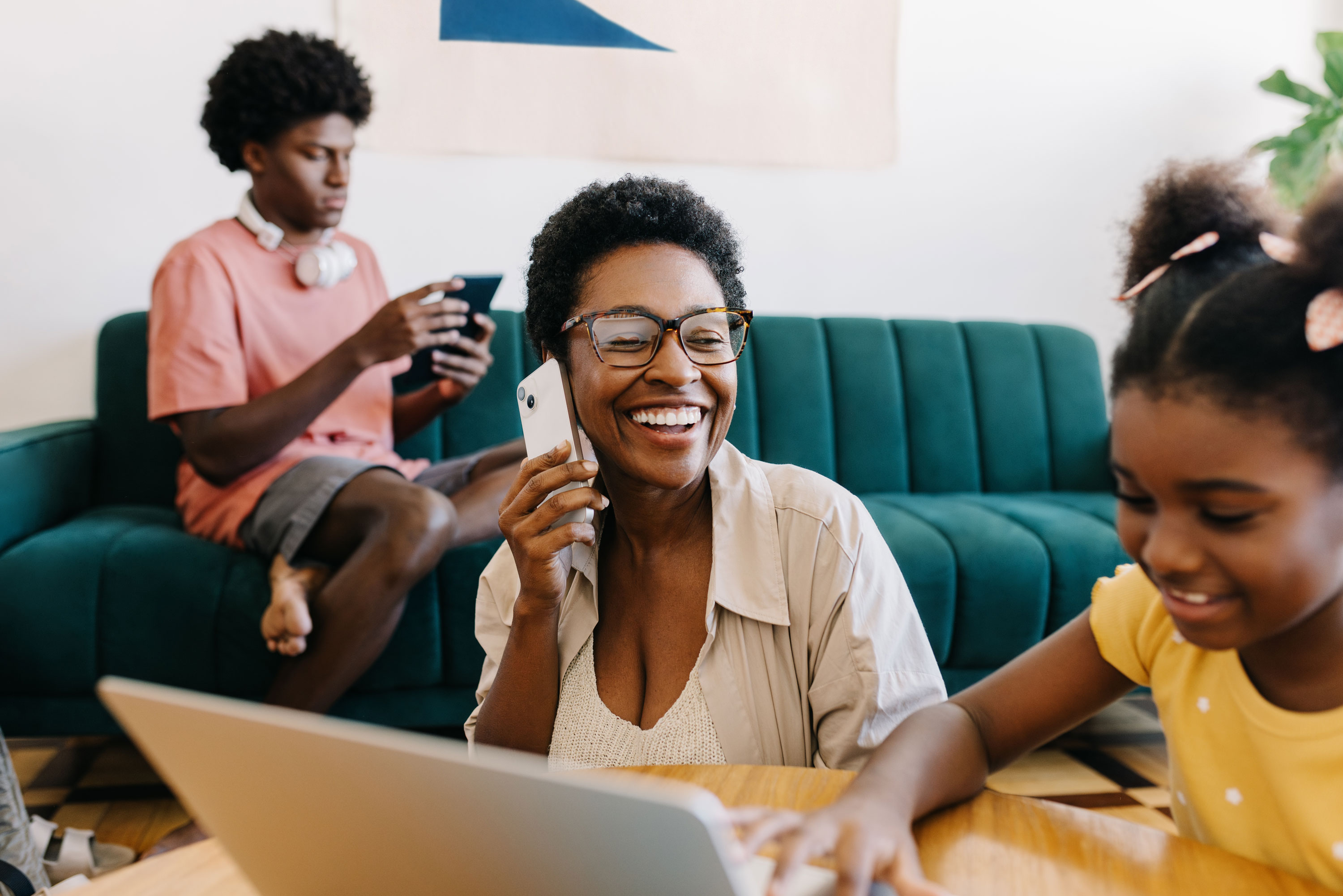 A mom smiles while on the phone in her living room surrounded by her two children.