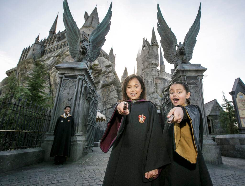 two young girls dressed like Hogwarts characters smile with wands at Universal Studios Hollywood in a Harry Potter area